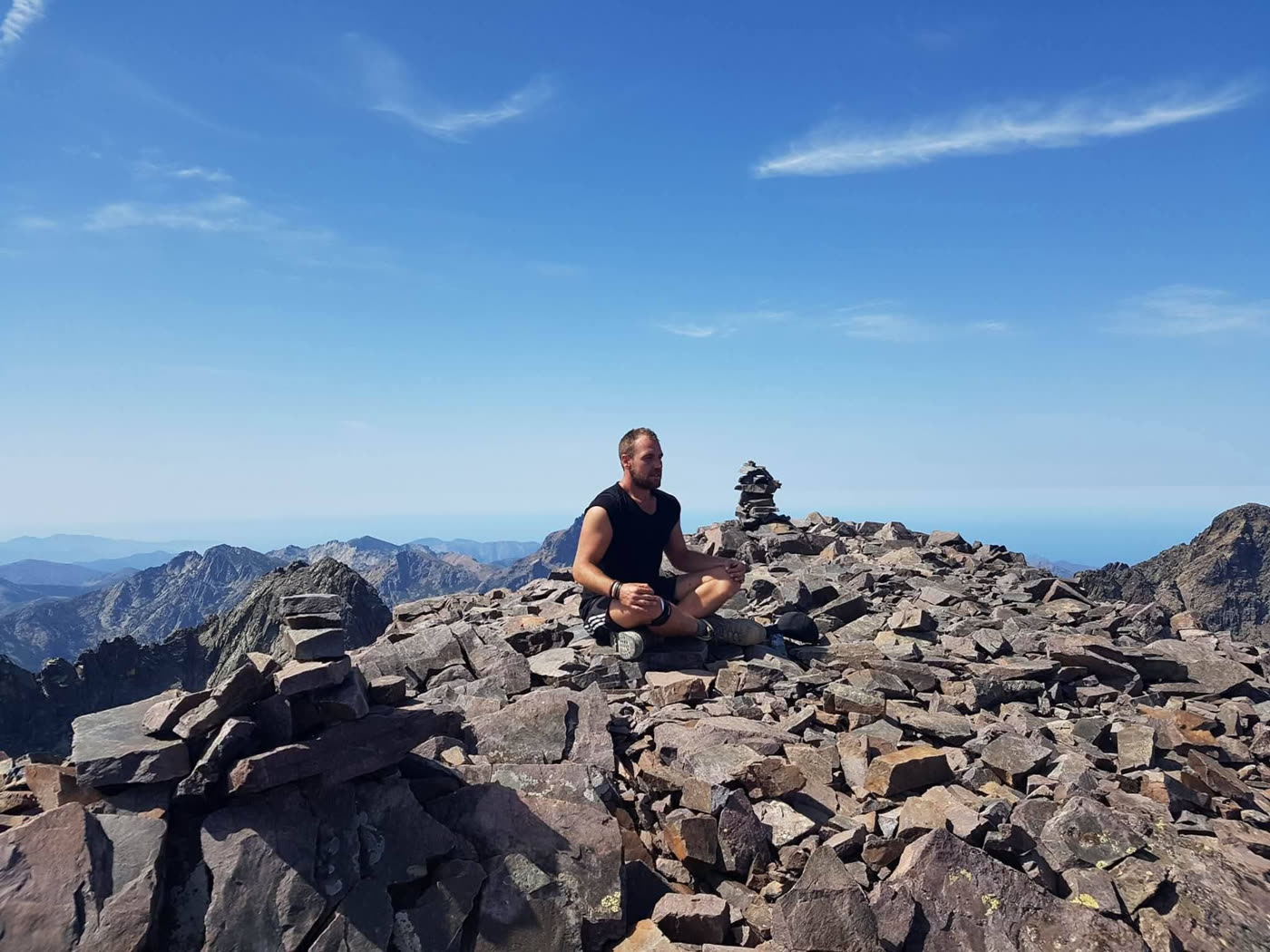 Kenneth zit in kleermakerszit op een rotsige bergtop onder een blauwe lucht